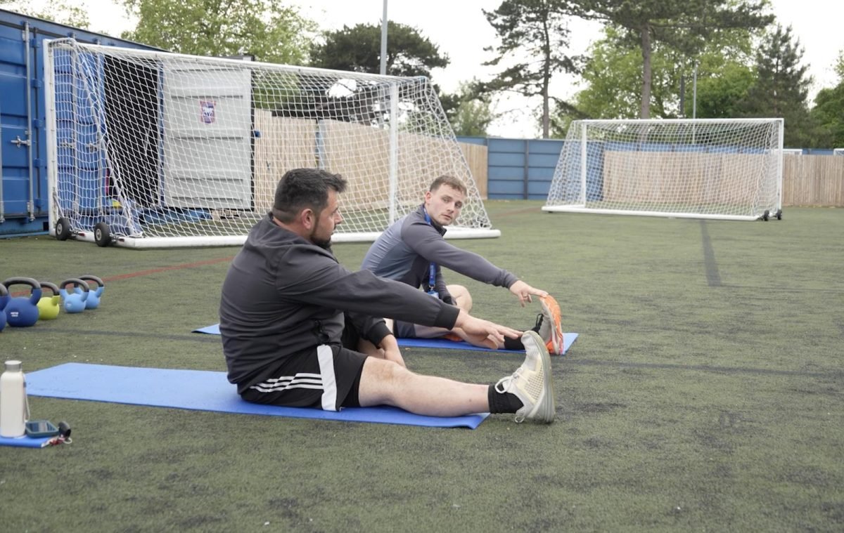 Two adults taking part in a guided exercise session on an outdoor sports pitch as part of the Active Blues health and wellbeing programme.