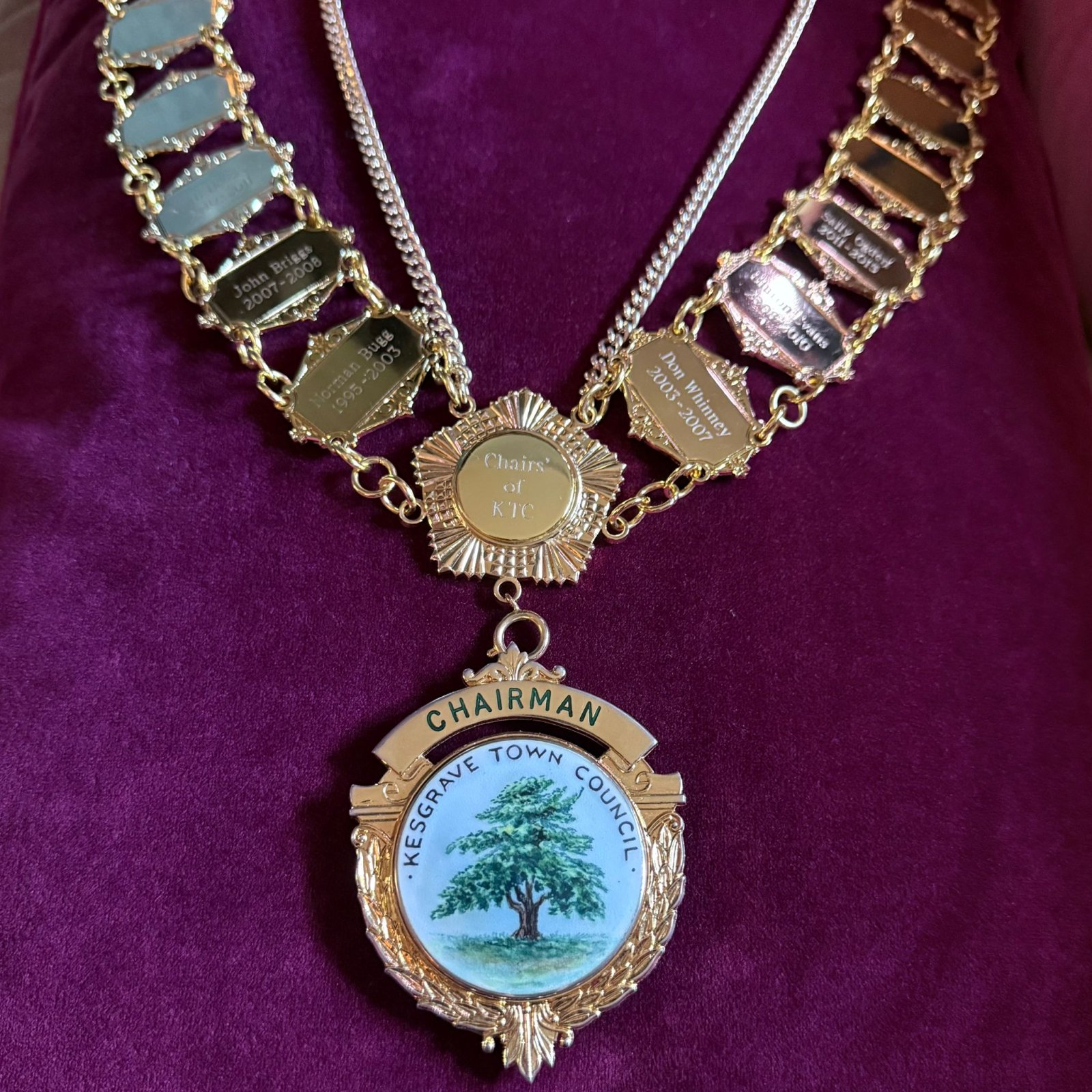 Close-up of the Kesgrave Town Council Chain of Office, showing the engraved gold pendant and links on a deep purple background.